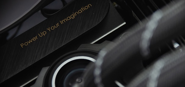 A close-up view of a mechanical or technological component with a sleek design and metallic textures is displayed. The phrase 'Power Up Your Imagination' is etched on the surface, suggesting encouragement or inspiration, possibly for creative or innovative activities.