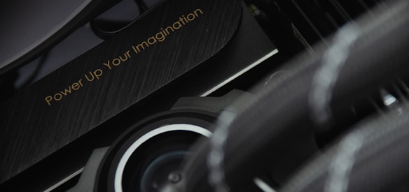 A close-up view of a mechanical or technological component with a sleek design and metallic textures is displayed. The phrase 'Power Up Your Imagination' is etched on the surface, suggesting encouragement or inspiration, possibly for creative or innovative activities.