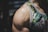 A close-up of a muscular person's shoulder wearing a floral-patterned tank top. The tank top features vivid green leaves and white flowers with subtle yellow accents. The focus is on the prominent veins and well-defined muscle on the shoulder.