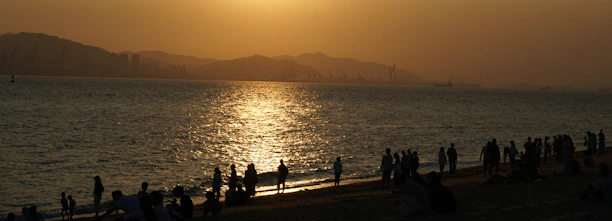 A vibrant beach scene at sunset with travelers enjoying the golden light and calm sea.