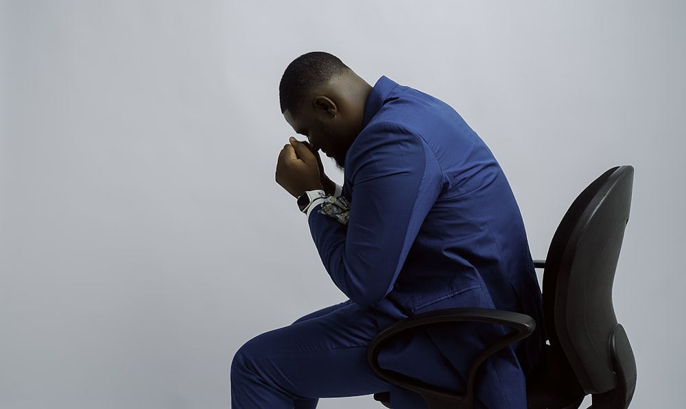 Un homme en costume bleu assis sur une chaise noire