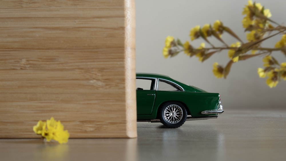 Un coche de juguete verde sentado junto a un jarrón con flores amarillas