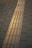 A sidewalk with a yellow tactile paving strip running through the middle, designed for visually impaired individuals. The paving consists of concrete tiles with a rectangular pattern, set against a darker background of regular paving stones.