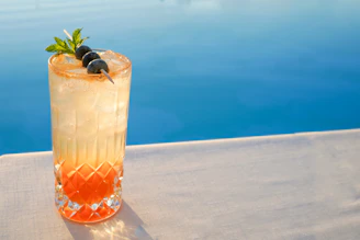 A refreshing cocktail served on a wooden tray beside the pool, with olive green accents in the background.