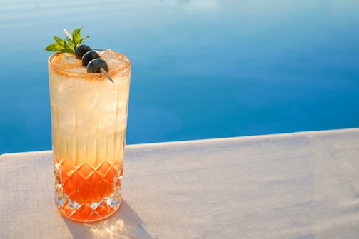 Close-up of a refreshing cocktail by the poolside with tropical plants in the background.
