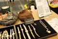 A display of wristwatches and jewelry is neatly arranged on a black velvet tray. Nearby, there are two leather bags, one black and one brown. A small sign reads 