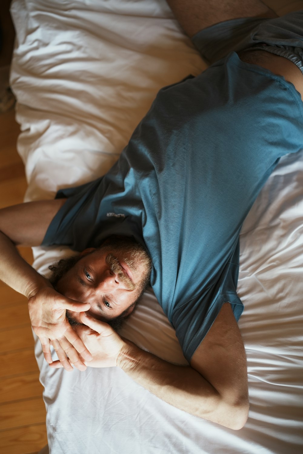 a man laying on top of a bed next to a wooden floor