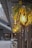 An artistic outdoor setting with decorative hanging lights. The lights are enclosed in wooden geometric frames and adorned with lush greenery and vibrant yellow flowers. This design creates a warm and inviting atmosphere along a wooden walkway, complemented by the soft glow of the bulbs.