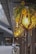 An artistic outdoor setting with decorative hanging lights. The lights are enclosed in wooden geometric frames and adorned with lush greenery and vibrant yellow flowers. This design creates a warm and inviting atmosphere along a wooden walkway, complemented by the soft glow of the bulbs.