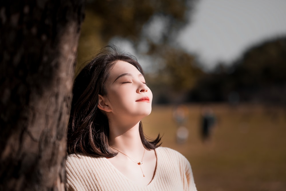 a woman standing next to a tree with her eyes closed