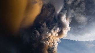 Volcanic eruption with dense plumes of dark and light ash against a backdrop of clear sky. The swirling clouds create a dramatic visual contrast and suggest intense natural activity.