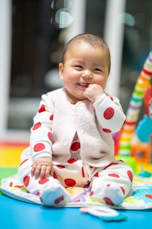 Smiling baby wearing cozy clothing sitting on a blanket.