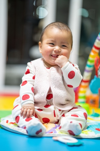 A smiling baby playing with safe, colorful toys on a soft blanket.