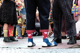 People are standing in a circle wearing colorful and mismatched socks with various patterns, such as hearts and stripes, paired with different types of shoes.