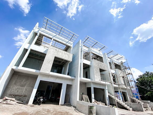 Several multi-story concrete structures are under construction, with visible scaffolding and unfinished surfaces. The sky is bright with scattered clouds.