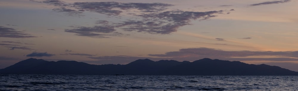 the sun is setting over the ocean with mountains in the distance