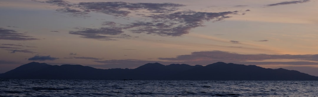 the sun is setting over the ocean with mountains in the distance,