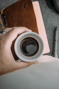 Hands writing notes beside a cup of coffee on a wooden desk.