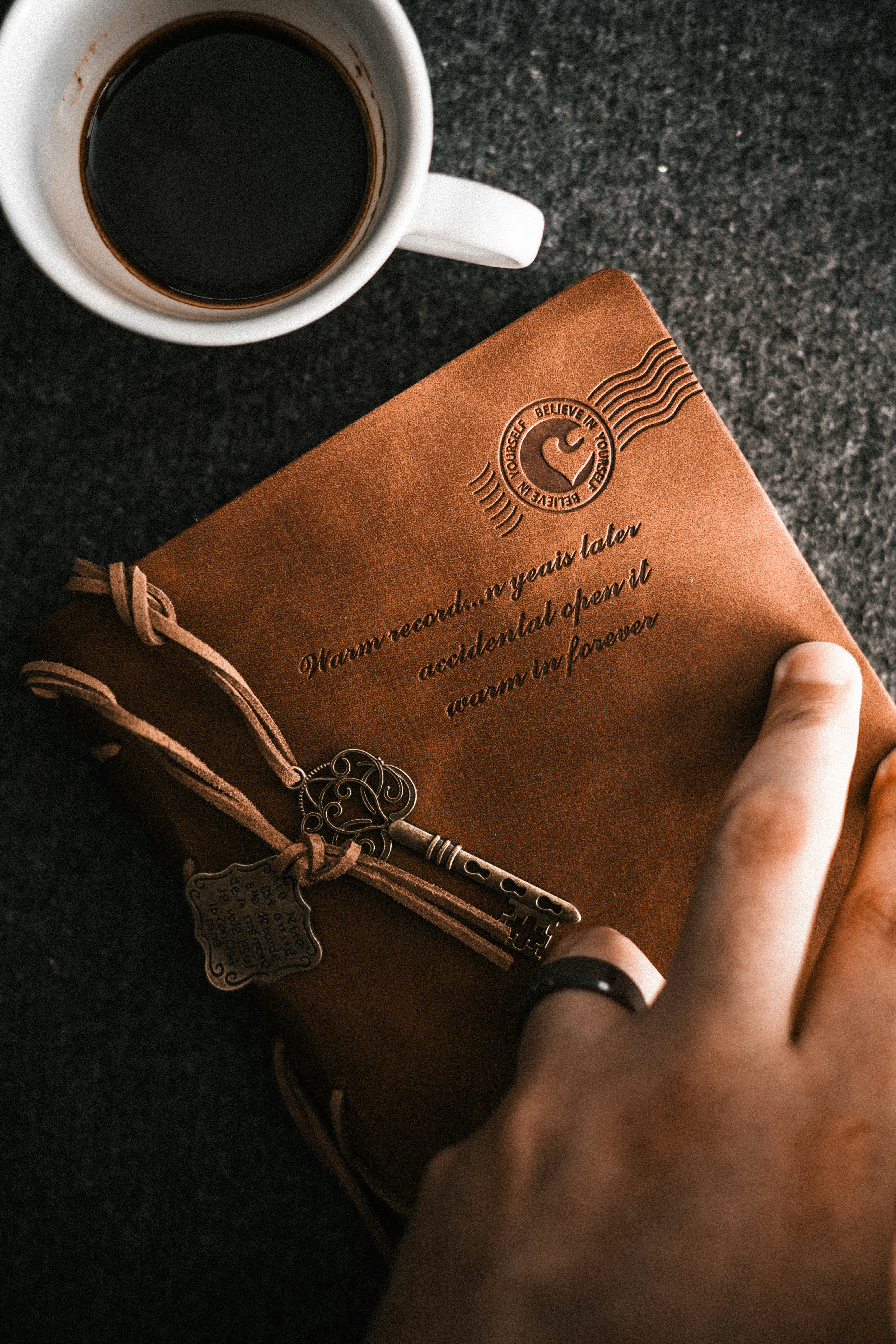 Una persona sosteniendo un libro marrón junto a una taza de café
