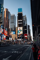 A bustling urban scene featuring tall skyscrapers adorned with bright billboards and advertisements. The street is busy with cars and pedestrians. Notable brands and colorful signs dominate the skyline, reflecting a vibrant, city atmosphere.