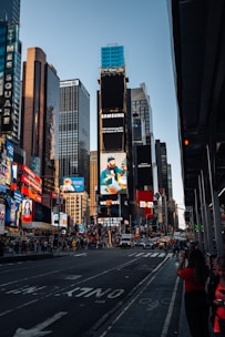 A bustling urban scene featuring tall skyscrapers adorned with bright billboards and advertisements. The street is busy with cars and pedestrians. Notable brands and colorful signs dominate the skyline, reflecting a vibrant, city atmosphere.