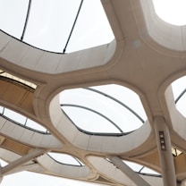 Futuristic architectural structure featuring large, circular, and interconnected concrete elements combined with transparent panels. Natural light filters through the glass, creating a modern and airy atmosphere.