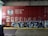A red freight train car covered with graffiti and the words 'Canadian Pacific Railway' prominently displayed. There are various tags and artistic designs in shades of white and blue on the train car. The setting appears to be inside a warehouse or an industrial area, with a metal roller door and a trash bin visible to the side. The floor consists of concrete with a yellow safety line along the edge.