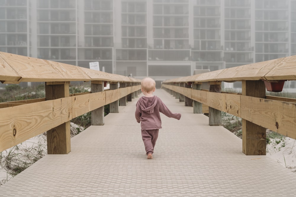 a little boy walking across a wooden walkway