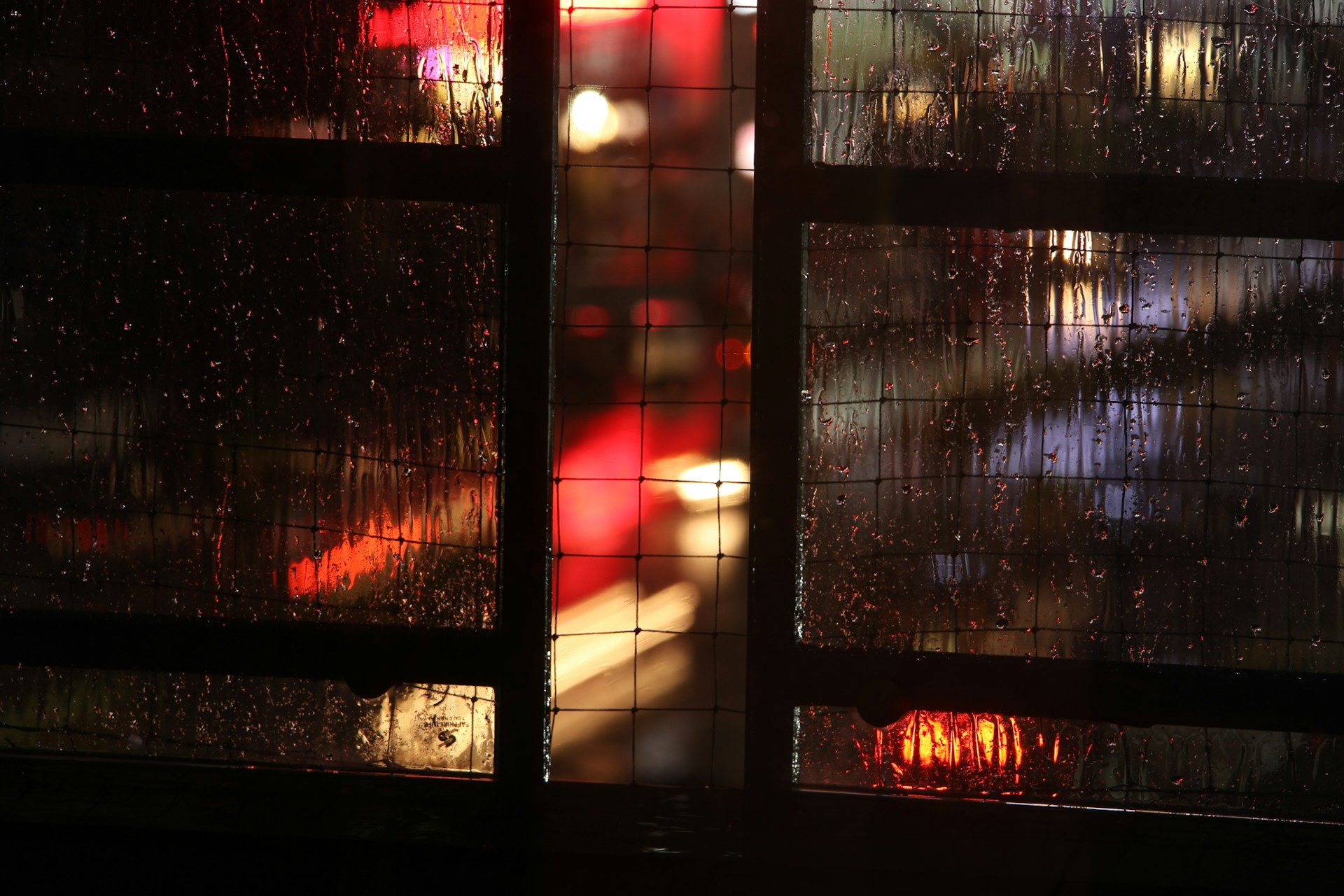 An atmospheric video still showing rain falling softly on a dark window, with blurred city lights glowing in the background.