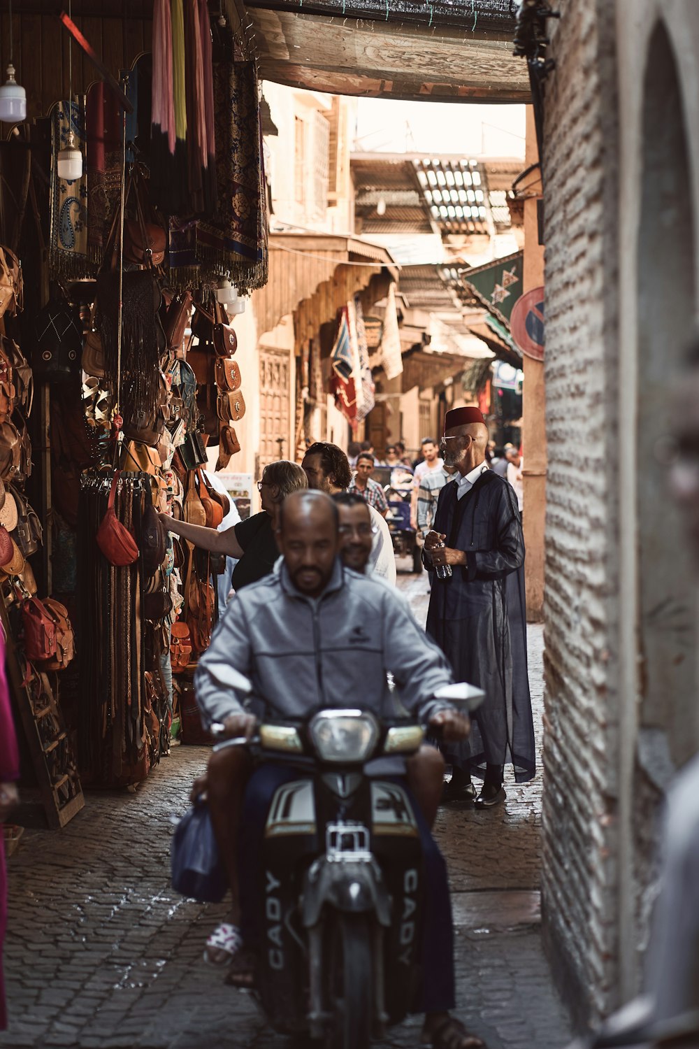 a man riding a motorcycle down a narrow street