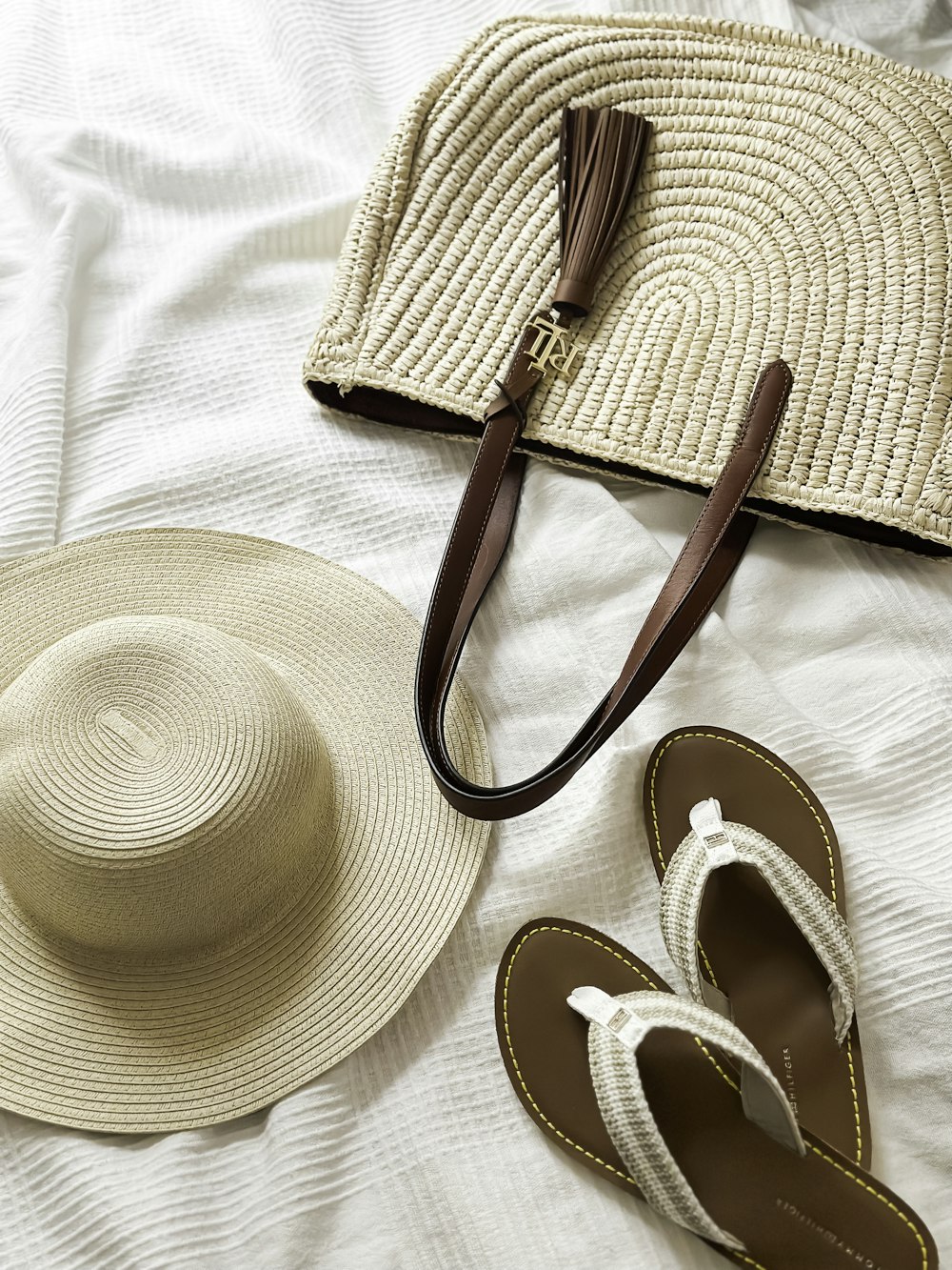 um chapéu, sandálias e uma bolsa em uma cama