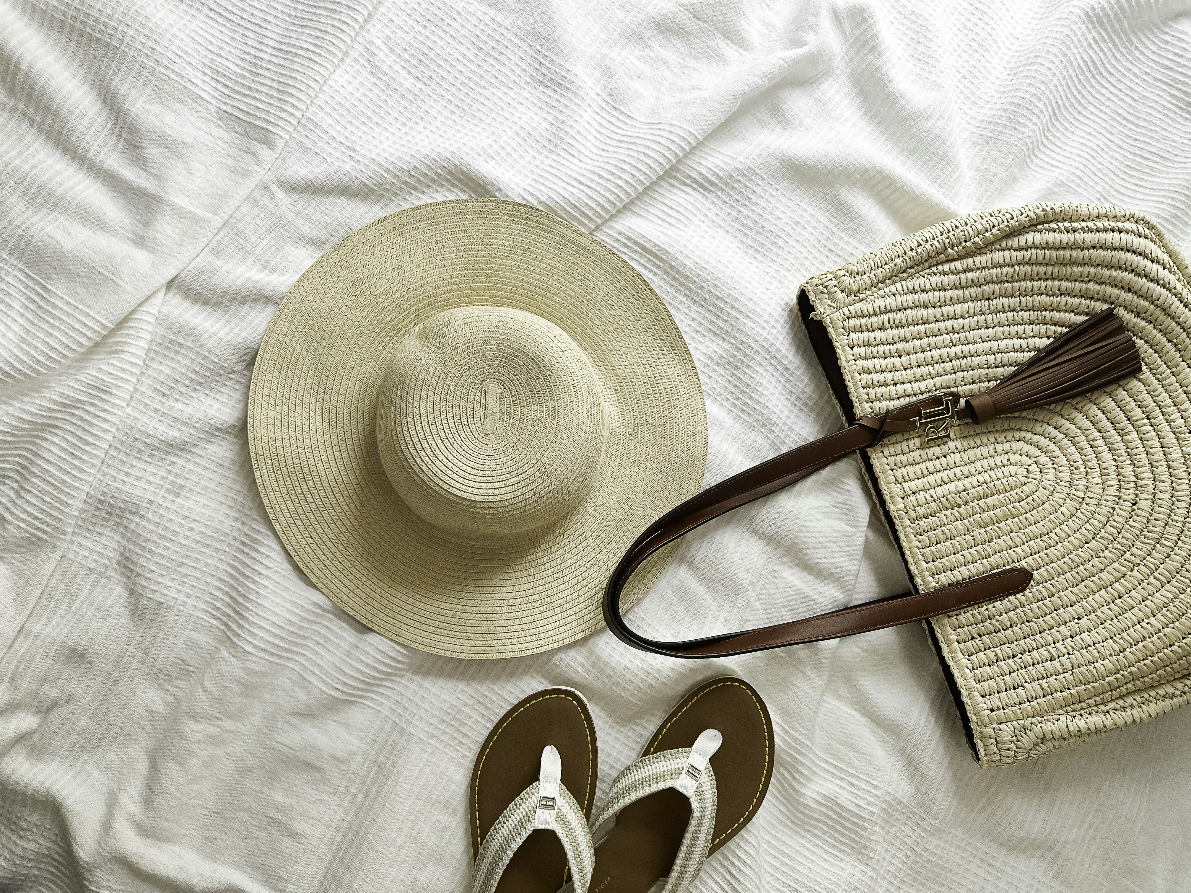 Stylish beachwear, including a sundress, sandals, and a sun hat, laid out on a bed - beach holiday packing list