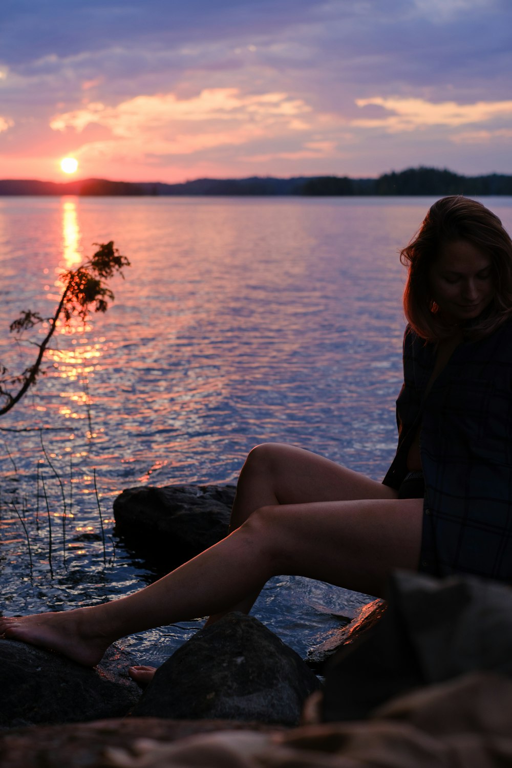 a woman sitting on a rock next to a body of water