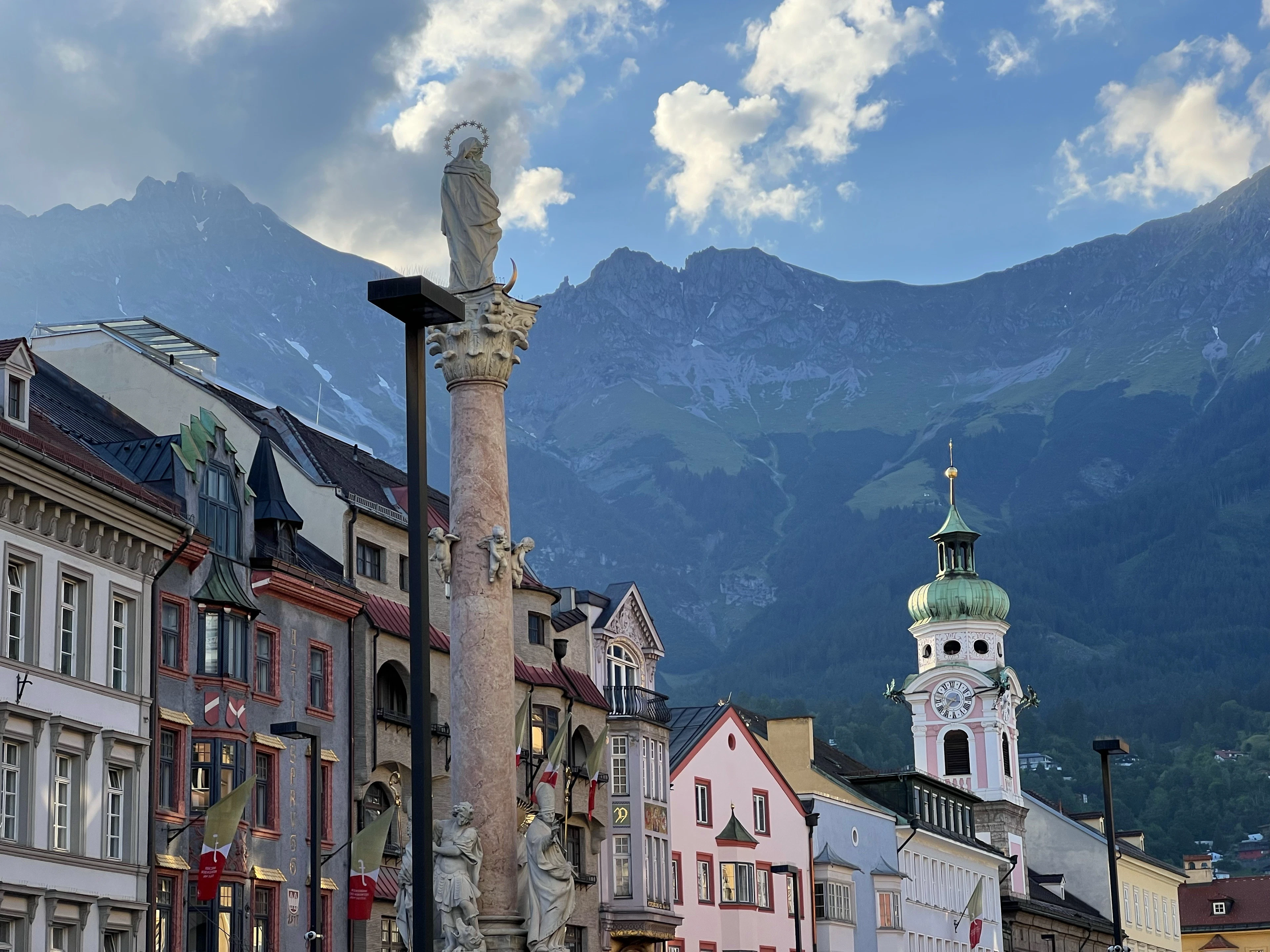 St. Anne's Column in Innsbruck's old town with a church tower and mountains behind under a dramatic sky.