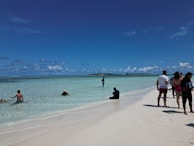 Tourists enjoying a sunny day on a sandy beach with clear blue water.