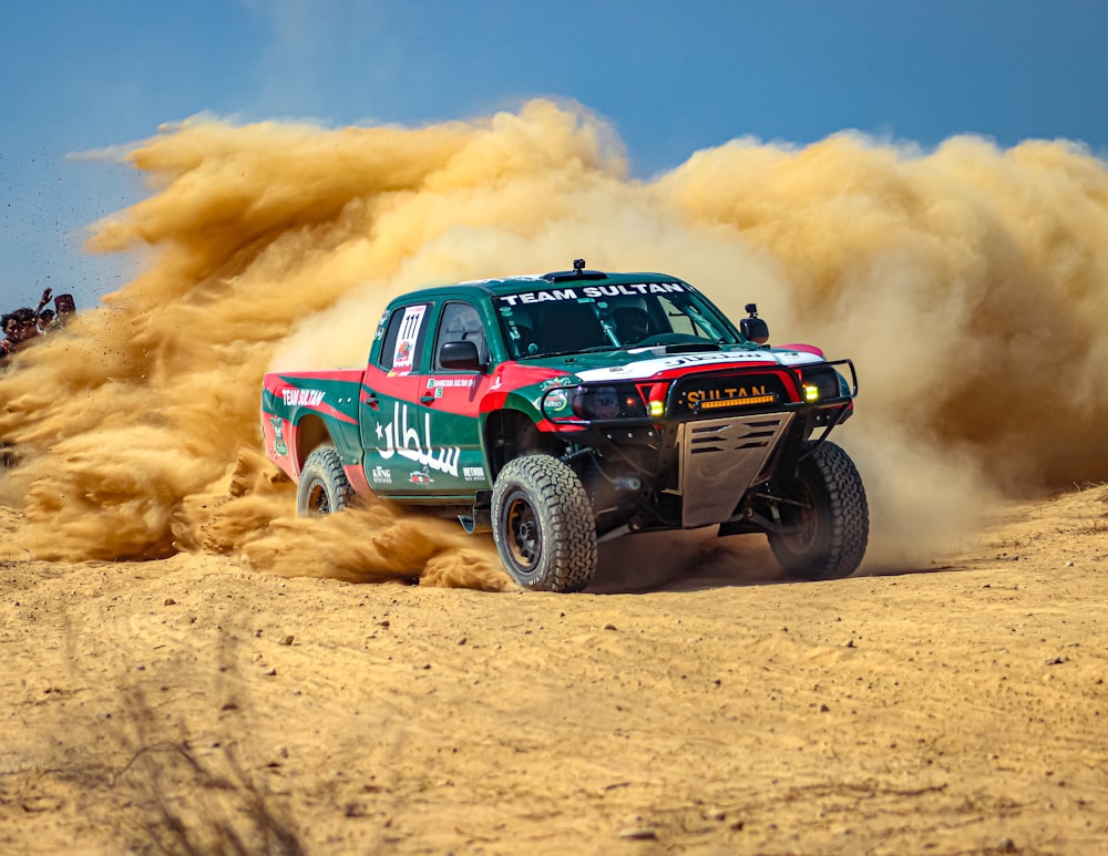 a green truck driving through a desert filled with dirt