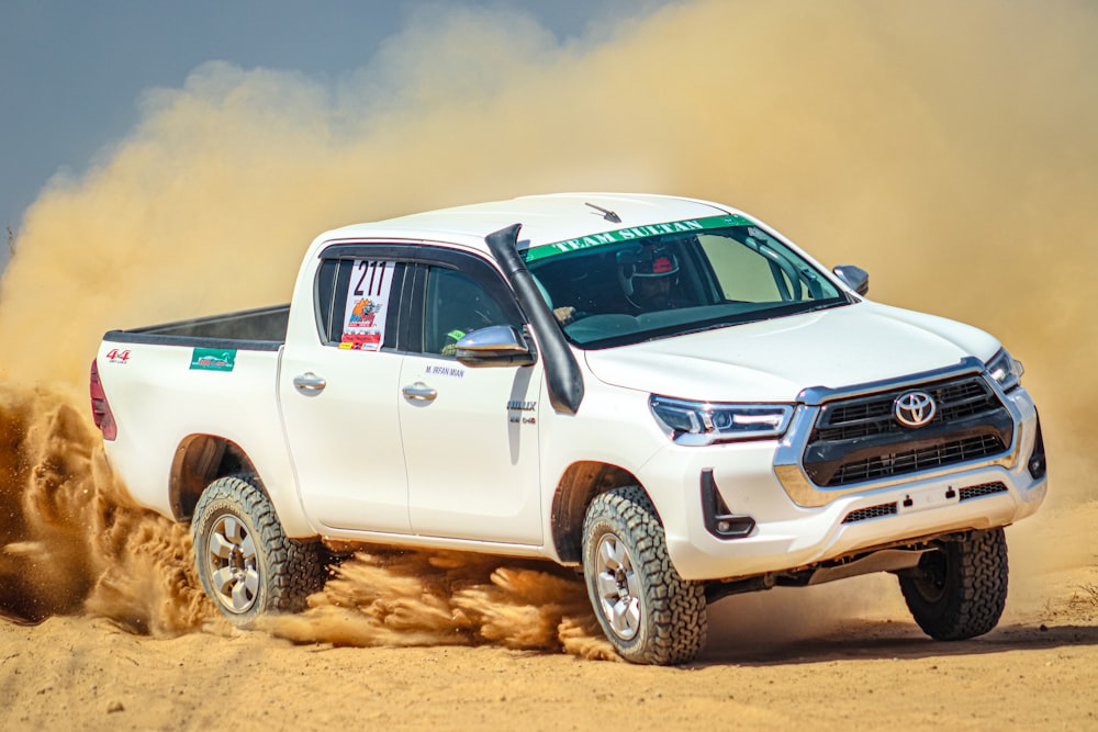 a white truck driving through a desert filled with sand