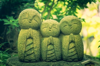 a group of three statues sitting on top of a moss covered rock