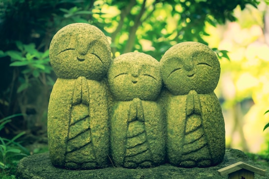 a group of three statues sitting on top of a moss covered rock