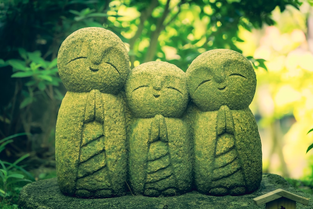 a group of three statues sitting on top of a moss covered rock