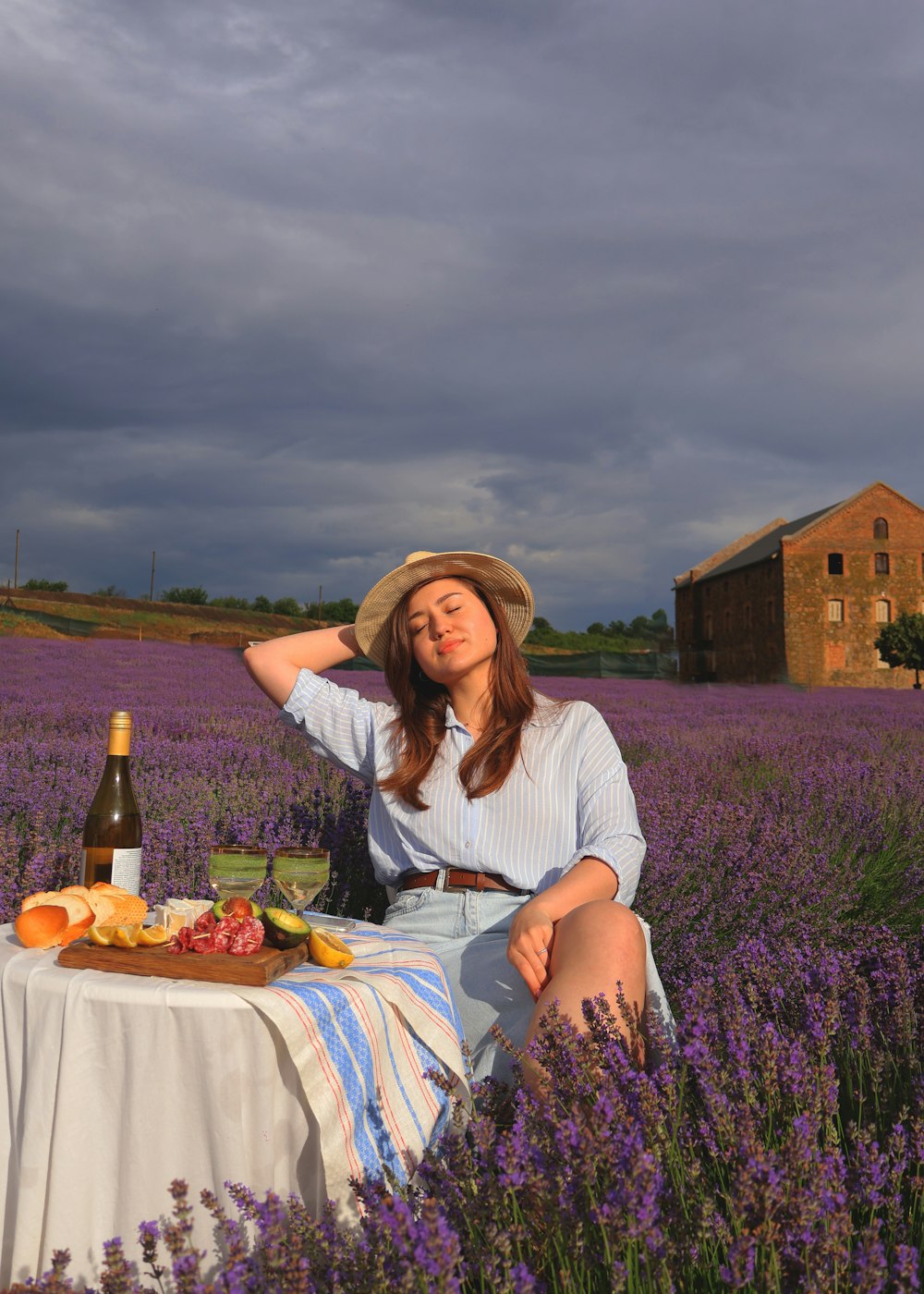 a woman sitting in a lavender field with a bottle of wine