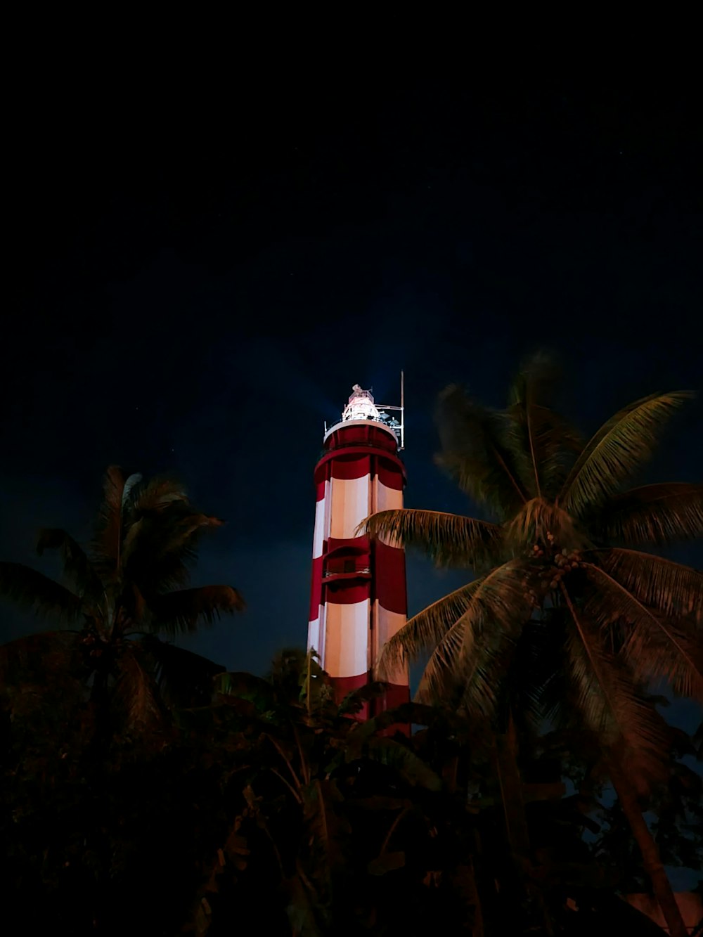 a tall red and white tower sitting next to palm trees