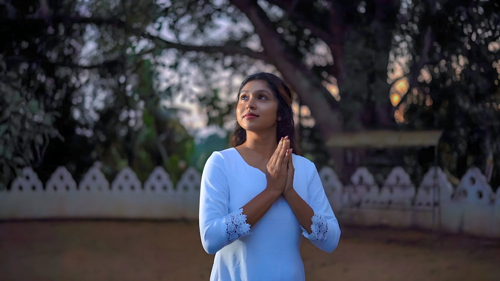 a woman standing in front of a tree and praying