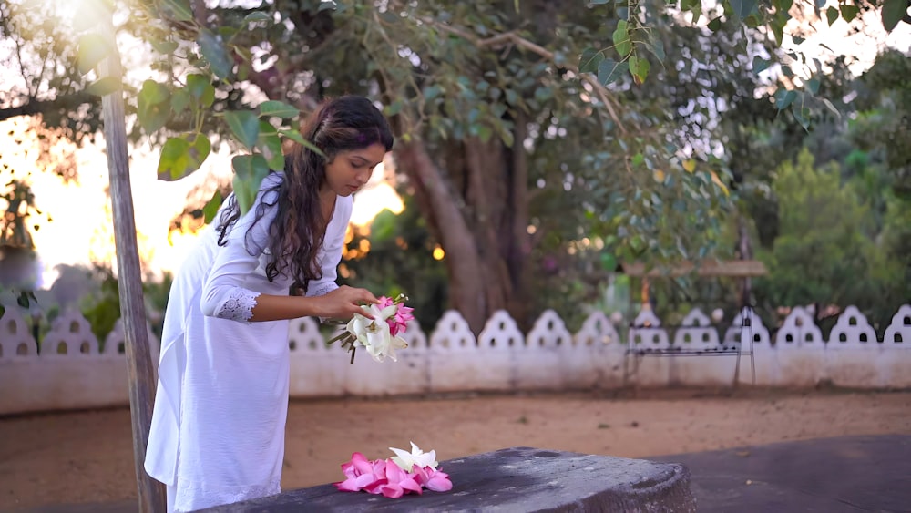 a woman placing flowers on a stone bench