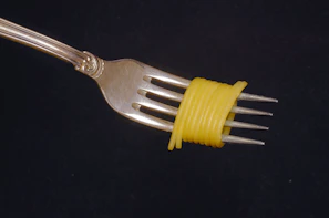 Close-up of perfectly portioned spaghetti twirled on a fork with a creamy sauce, set against a minimalist cream and pasta yellow background.