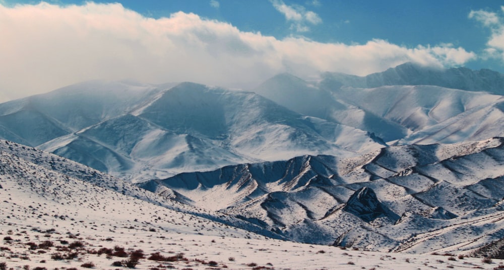 a mountain range covered in snow under a cloudy sky