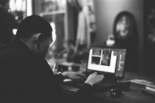 A person browsing a laptop, surrounded by various household products and gadgets, appearing thoughtful and focused.
