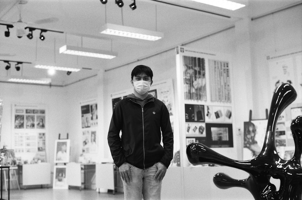 a man wearing a face mask standing next to a sculpture