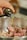 A hand is pouring oil from a dark bottle into a bowl containing raw meat pieces.