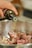 A hand is pouring oil from a dark bottle into a bowl containing raw meat pieces.